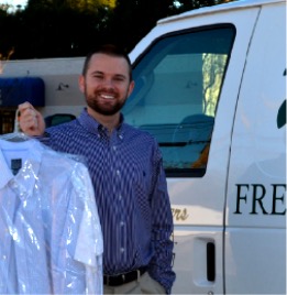 A Waite's Cleaners team member holding freshly cleaned shirts beside the free pickup and delivery van