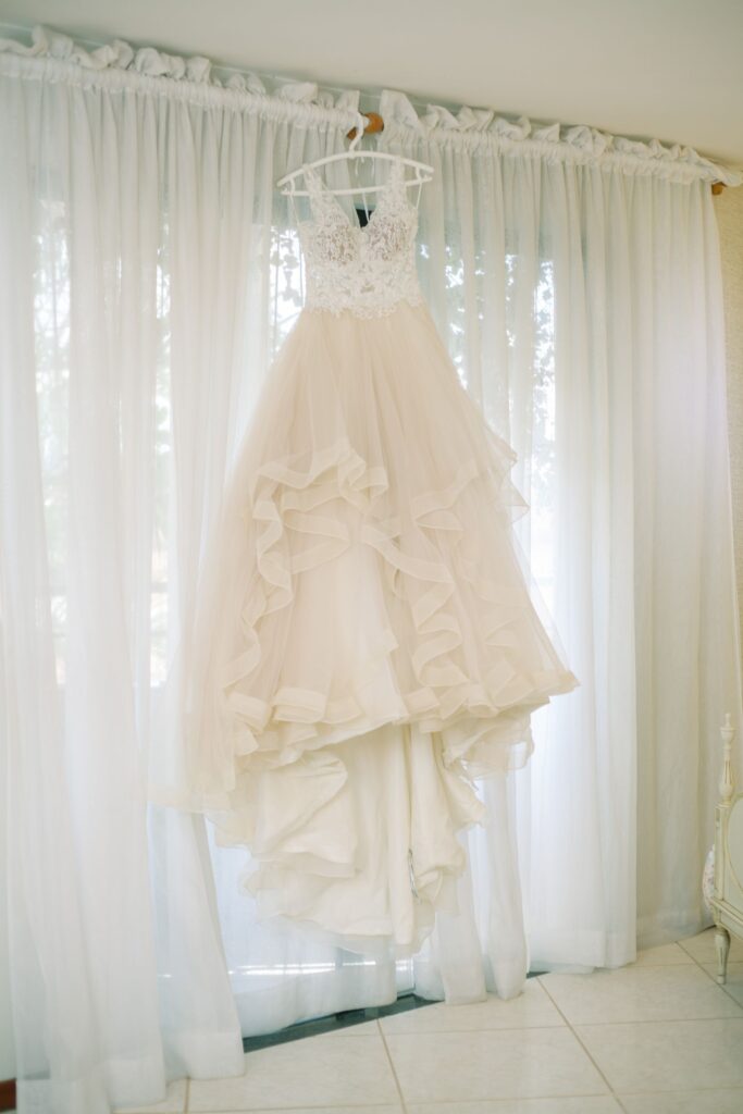 A lace wedding gown hanging in a sunlit room