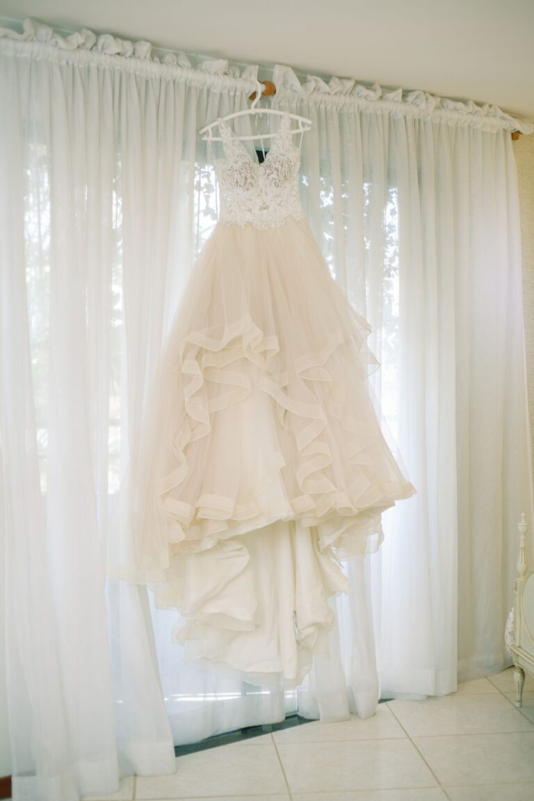 A lace wedding gown hanging in a sunlit room